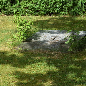 Bild vergr&ouml;&szlig;ern: Abgebildet ist eine in den Rasen eingelassene Grabplatte im Halbschatten.